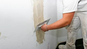 Persona que utiliza una paleta para aplicar yeso a una pared en un entorno interior.