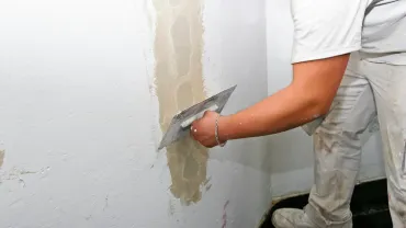 Persona que utiliza una paleta para aplicar yeso a una pared en un entorno interior.