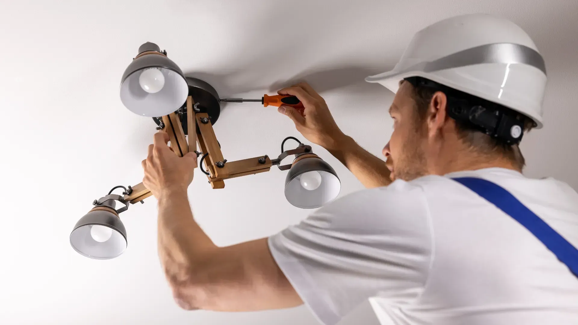 Persona con casco instalando una lámpara de techo con un destornillador.