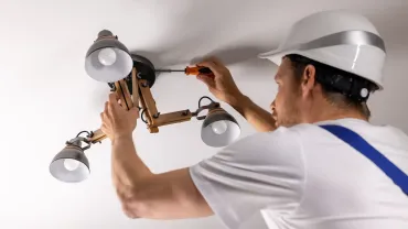 Persona con casco instalando una lámpara de techo con un destornillador.