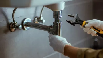 Manos con guantes blancos utilizando una llave inglesa para reparar la plomería del lavabo del baño.