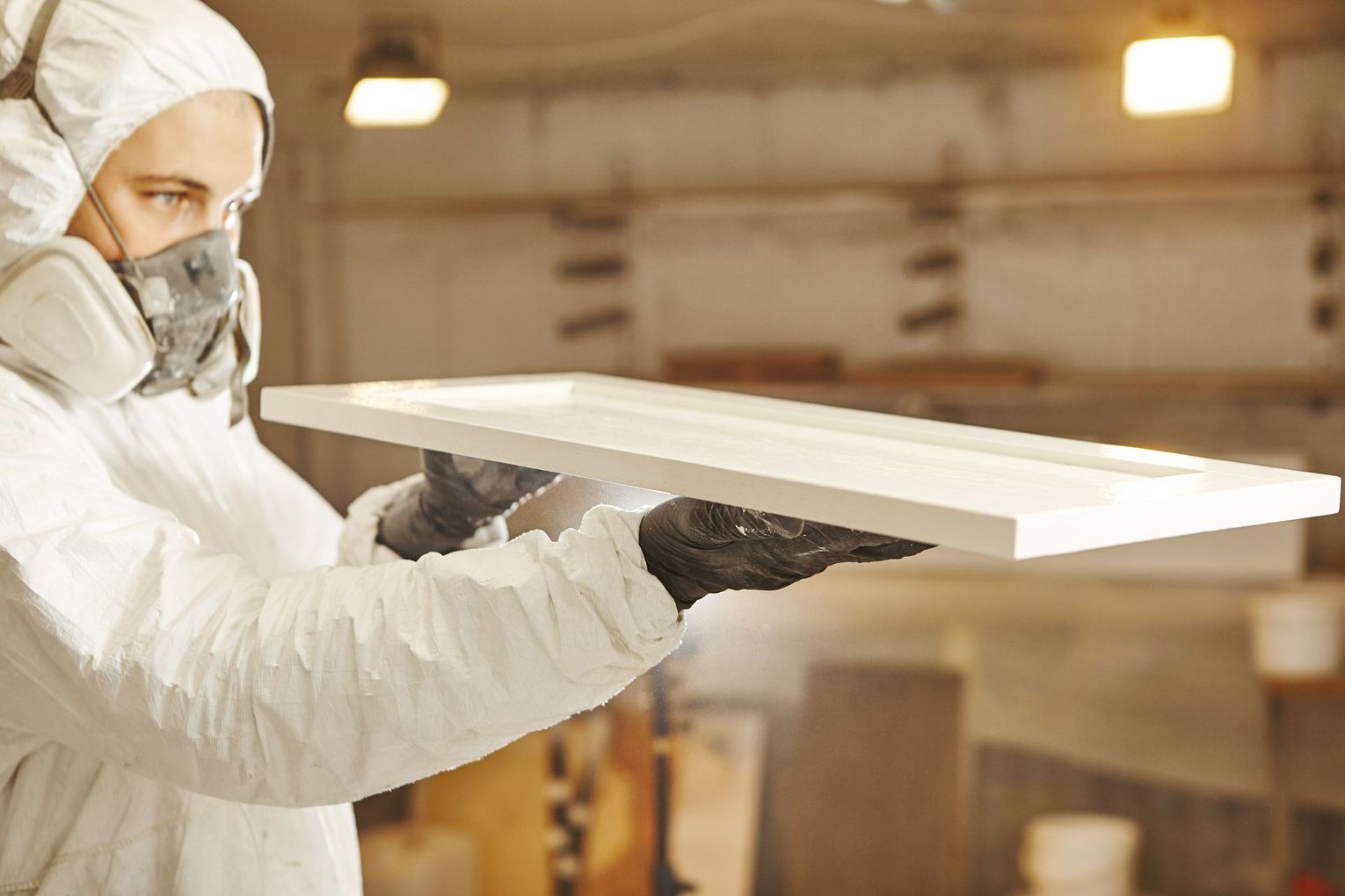 Artisan portant un eplanche en bois blanche avec des gants
