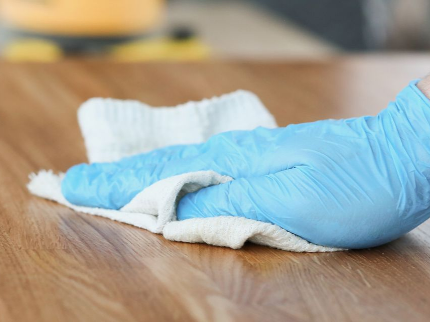 Une main gantée essuie une surface en bois avec un chiffon blanc