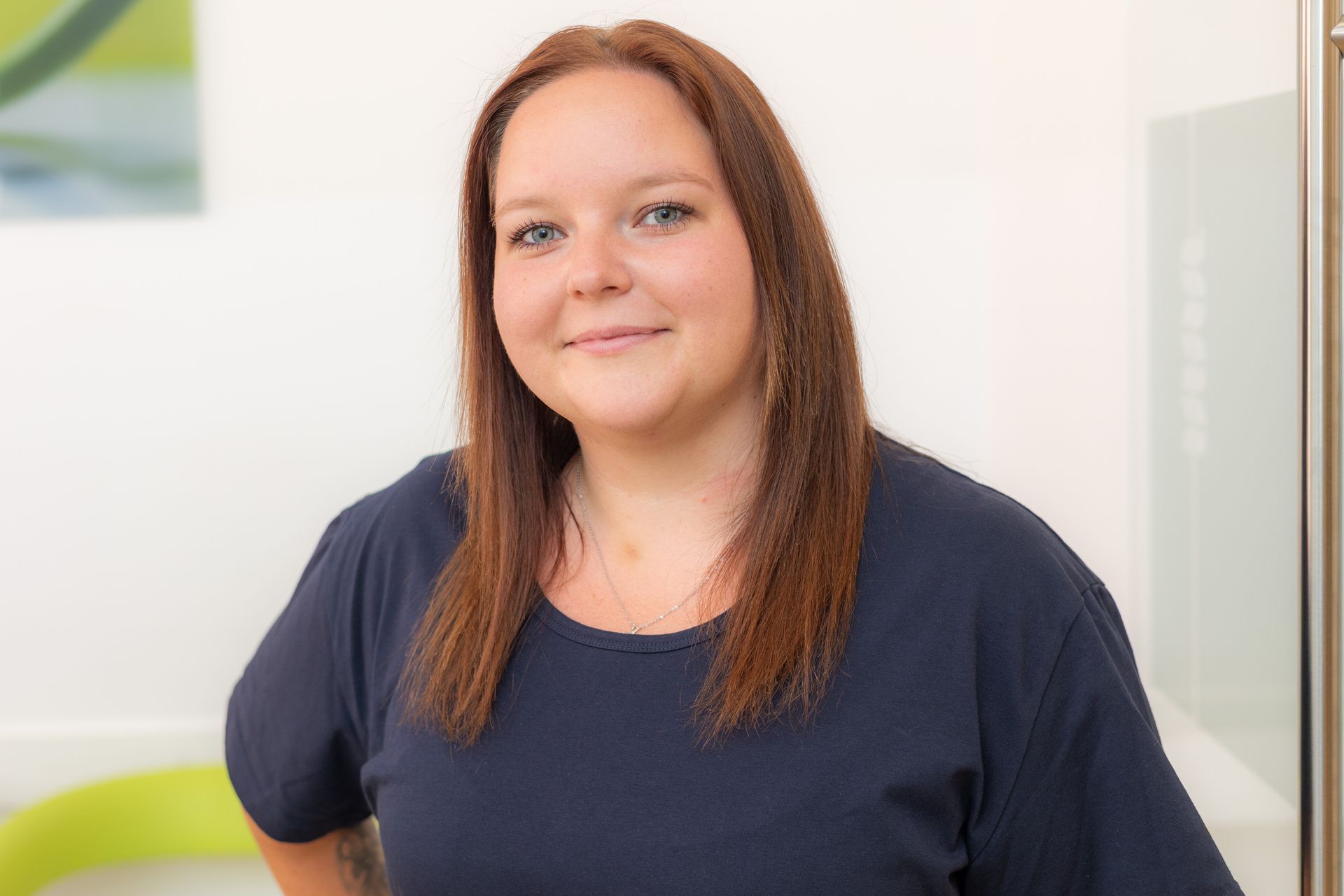 Frau mit kastanienbraunem Haar, trägt ein dunkelblaues Hemd und lächelt in die Kamera.