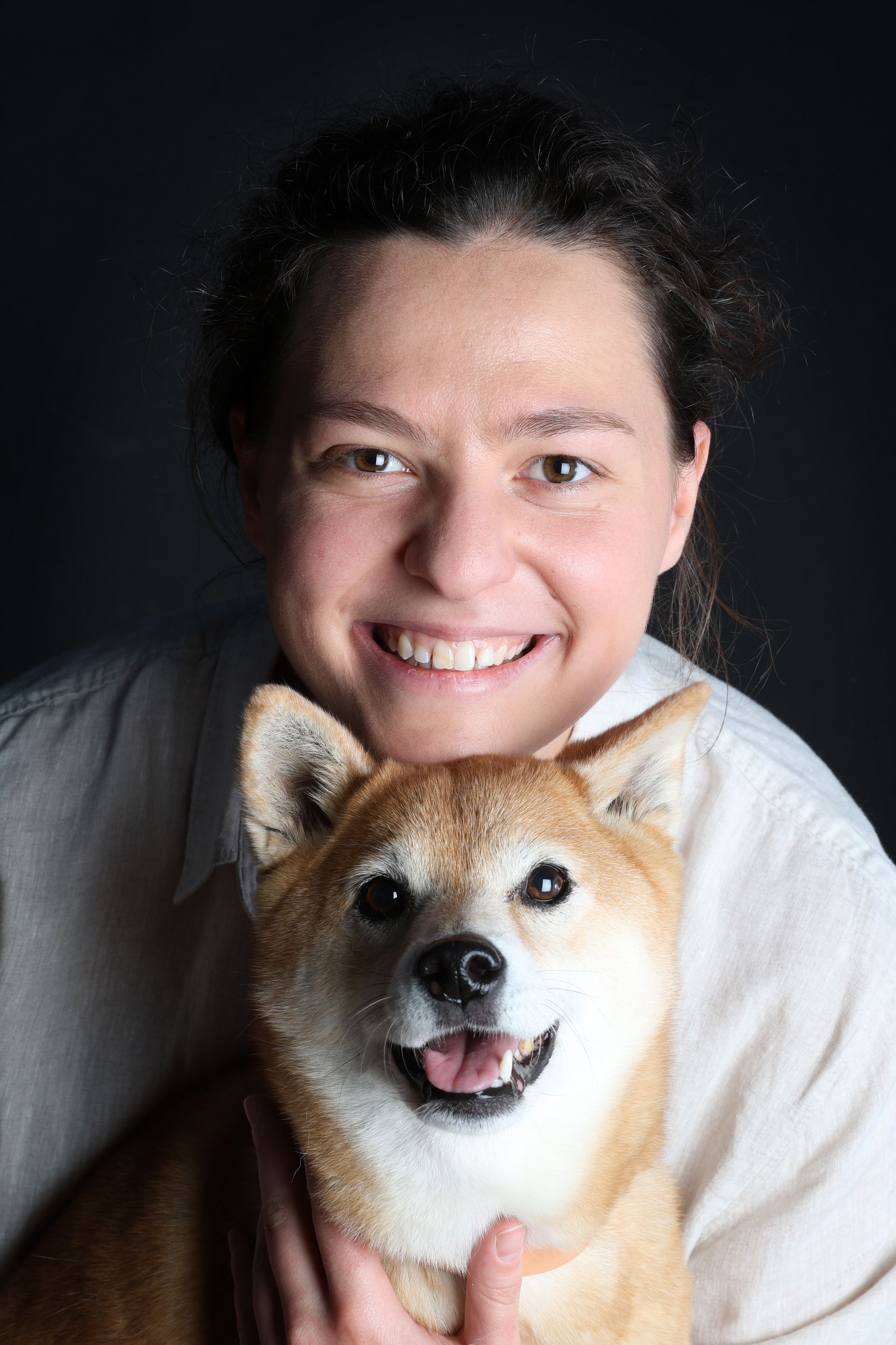 Personne souriante tenant un chien Shiba Inu couleur fauve sur un fond sombre