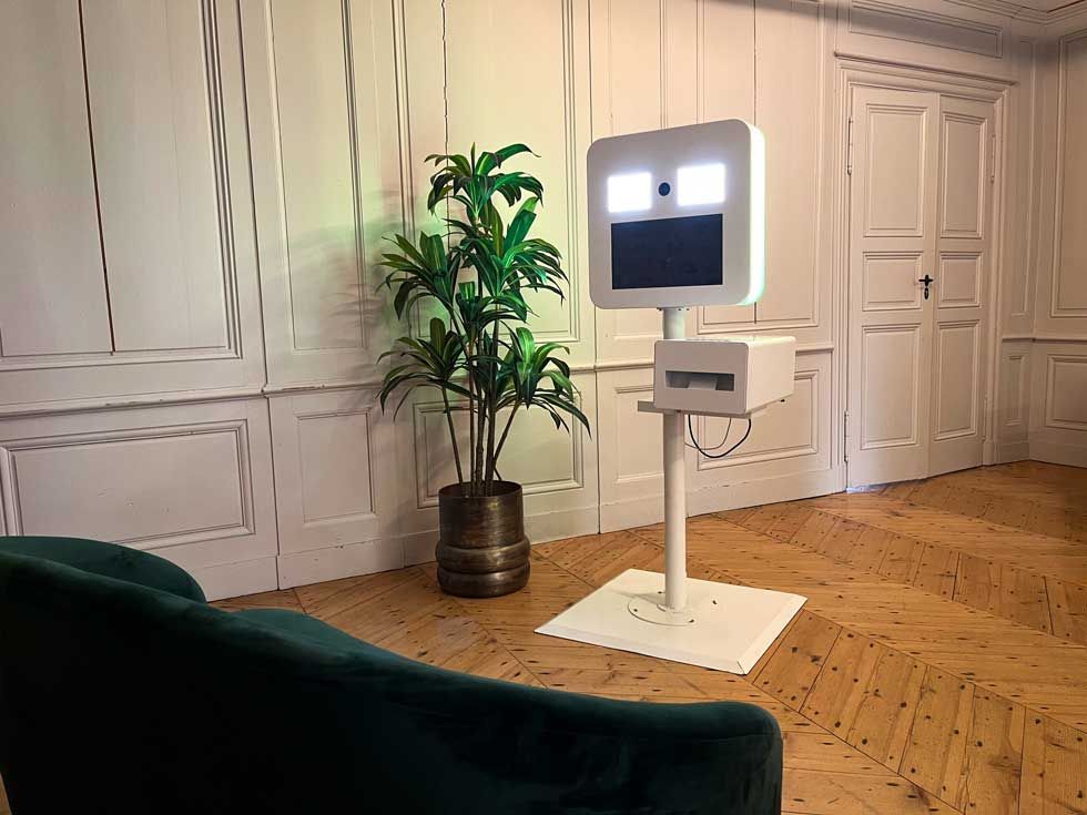 Robot de téléprésence dans un salon moderne, à côté d’une plante en pot et d’un canapé vert
