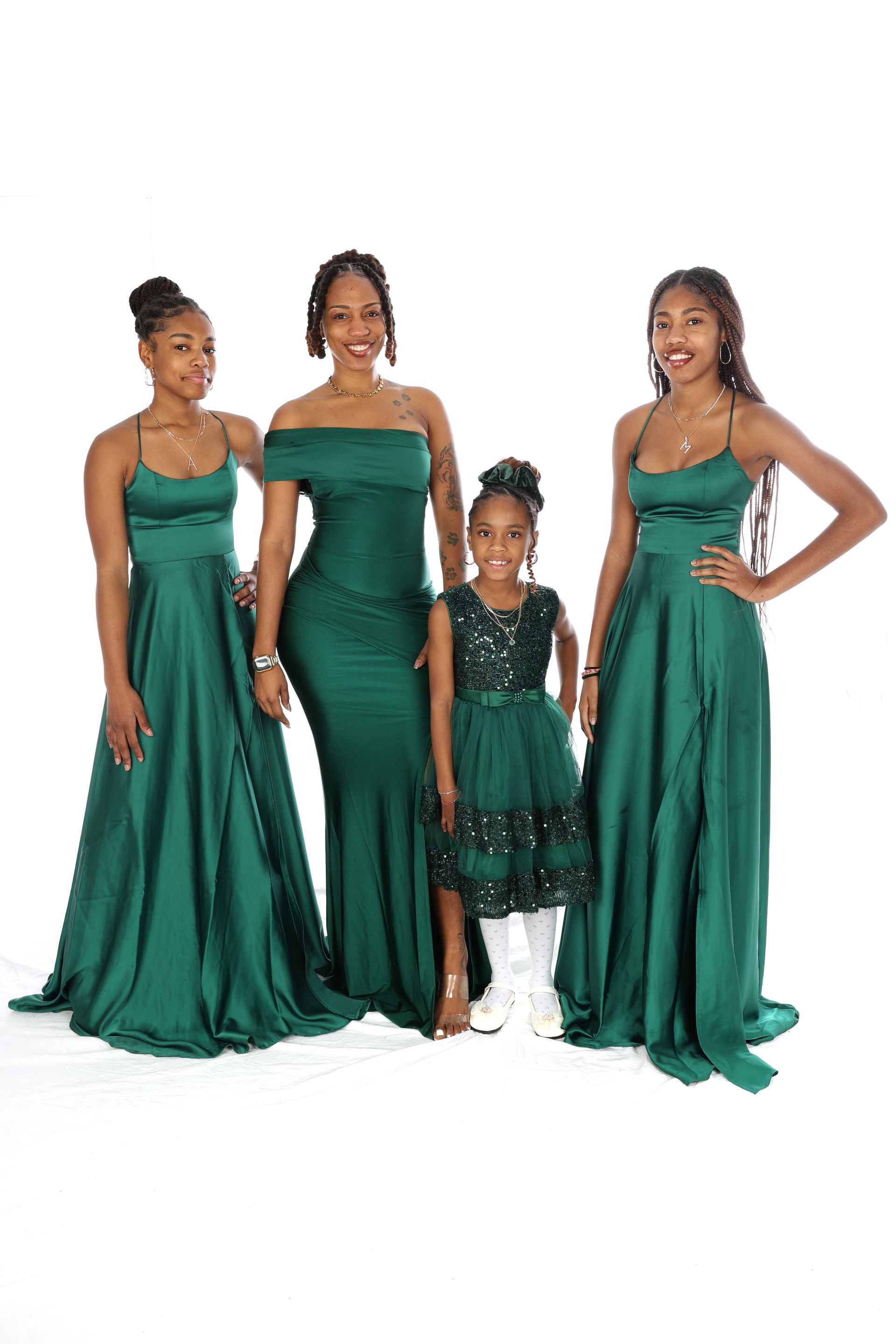 Quatre femmes en robes de soirée vert émeraude assorties, posant sur un fond blanc