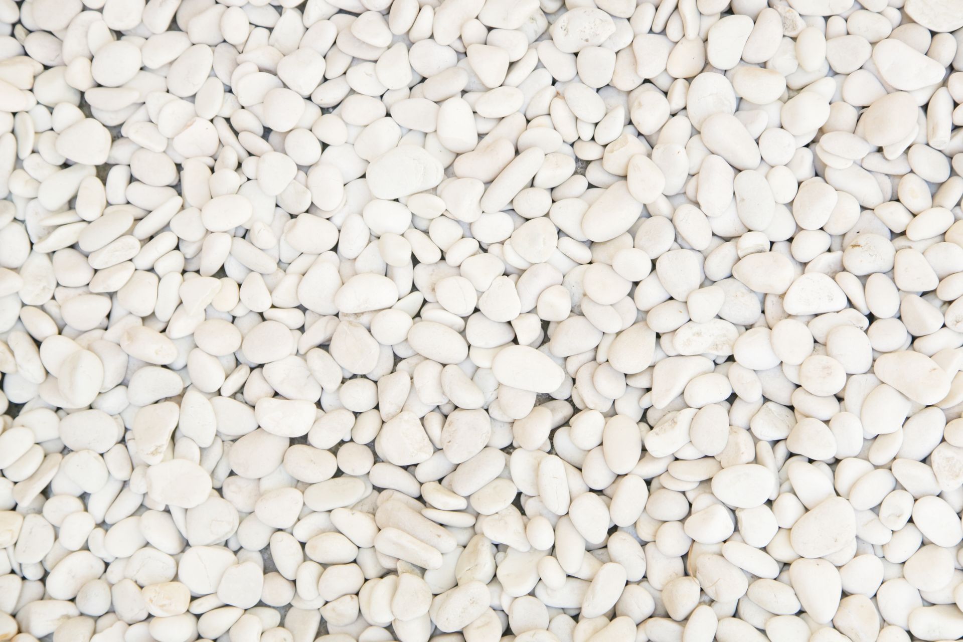 Gros plan sur de nombreux petits galets décoratifs lisses, blanc cassé, recouvrant l'intégralité du cadre.