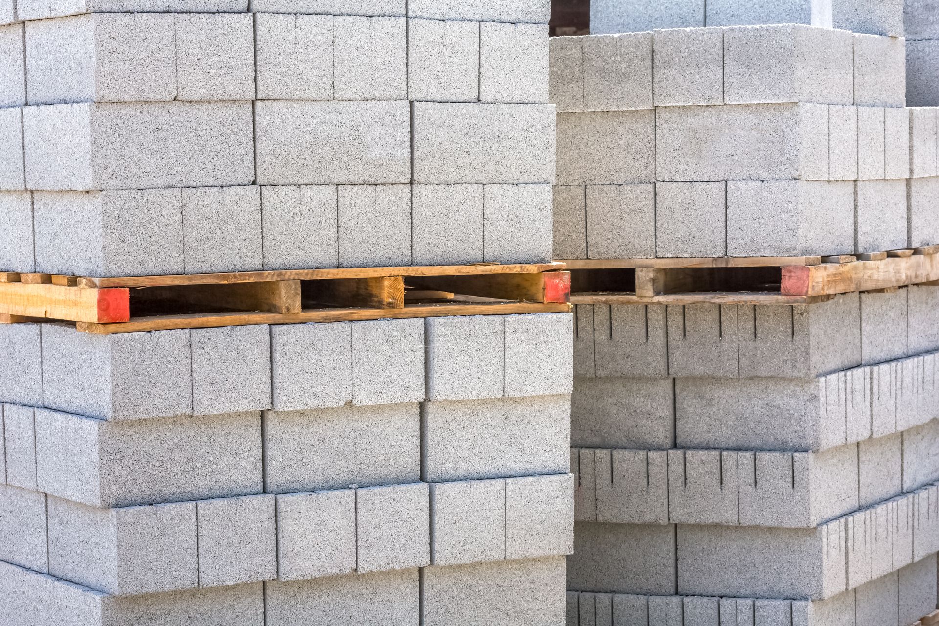 Deux piles d'éléments de maçonnerie en béton gris soigneusement disposés sur des palettes en bois.