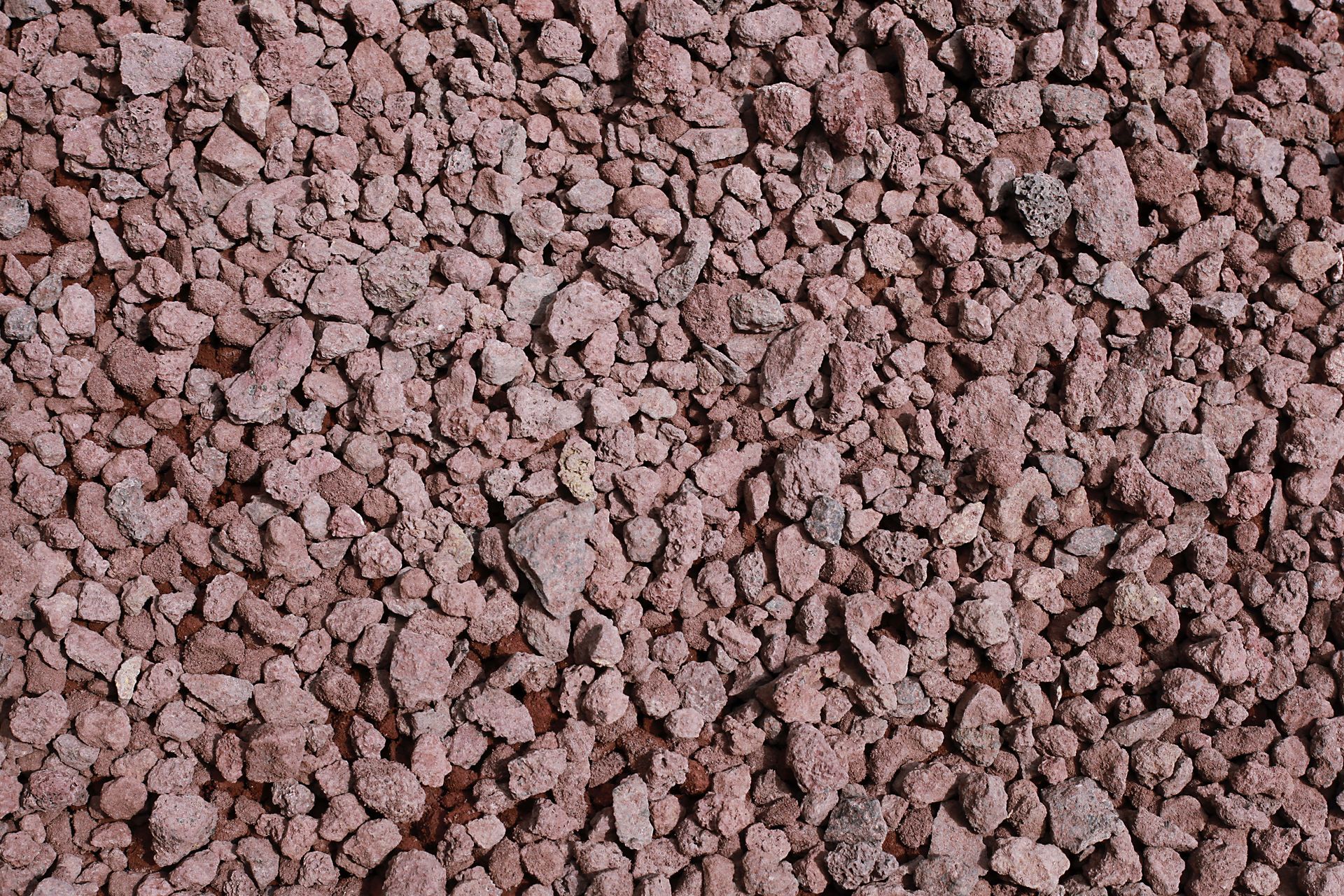 Gros plan sur des morceaux de roche volcanique rouge concassée, à la texture poreuse et irrégulière.