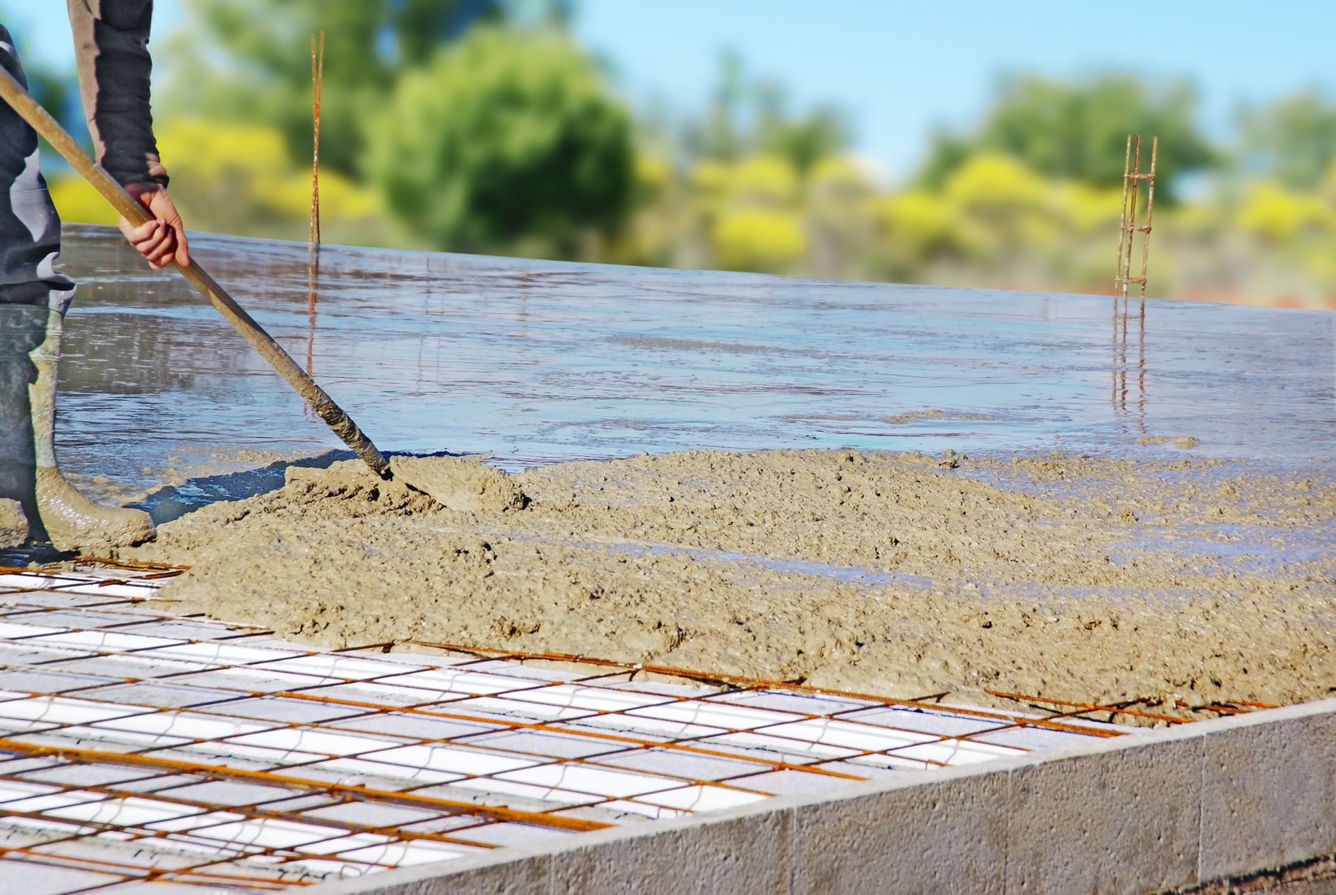 Un ouvrier du bâtiment utilise un râteau pour étaler du béton frais sur un treillis métallique posé sur une fondation.