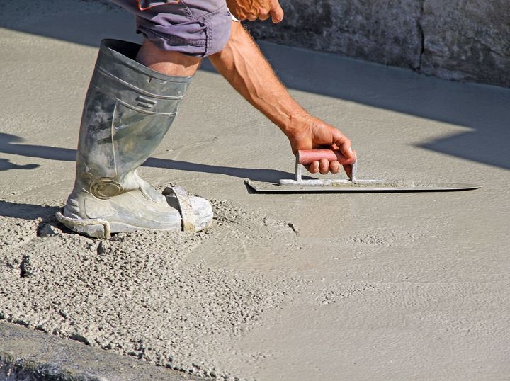 Homme qui étale du béton au sol.