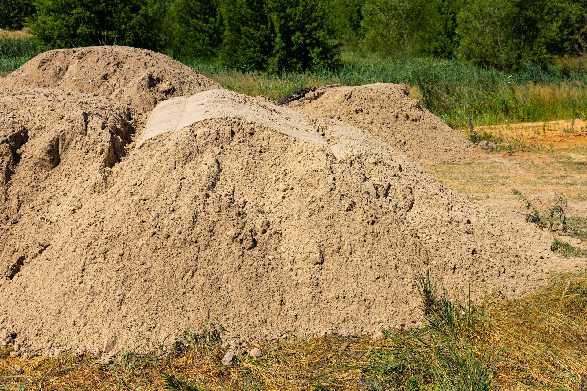 Un grand monticule irrégulier de sable grossier brun clair se dresse au milieu d'un champ ouvert, sur fond d'arbres et d'herbe verts.
