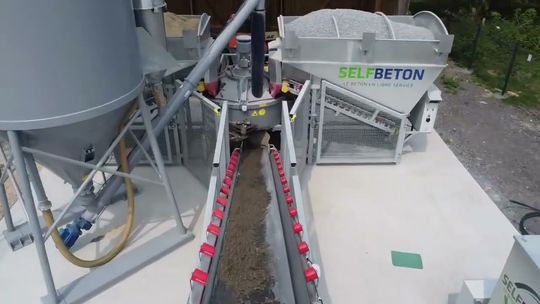 Une centrale à béton avec un silo de stockage et un système de convoyeur à bande distribuant les granulats mélangés.