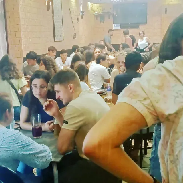 Gente en un bar; gente sentada en mesas, conversando. Iluminación tenue, paredes de ladrillo y adornos colgantes.