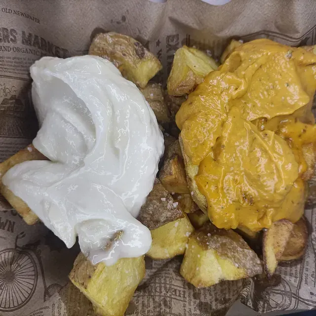 Patatas asadas con salsa blanca y salsa de naranja en una cesta forrada de papel de periódico.