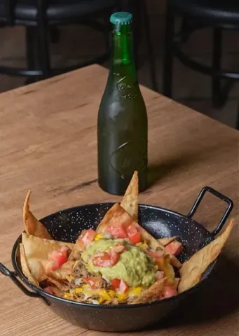 Nachos con guacamole y una botella de cerveza sobre una mesa de madera.