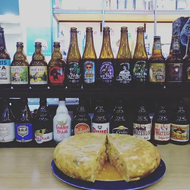 Una tortilla cortada en un plato con filas de botellas de cerveza detrás de ella.