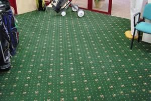 Un suelo alfombrado verde con bolsas de golf y una silla.
