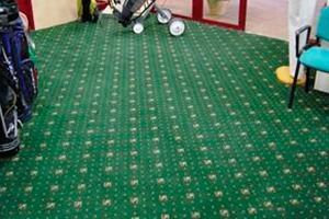Un suelo alfombrado verde con una bolsa de golf encima.