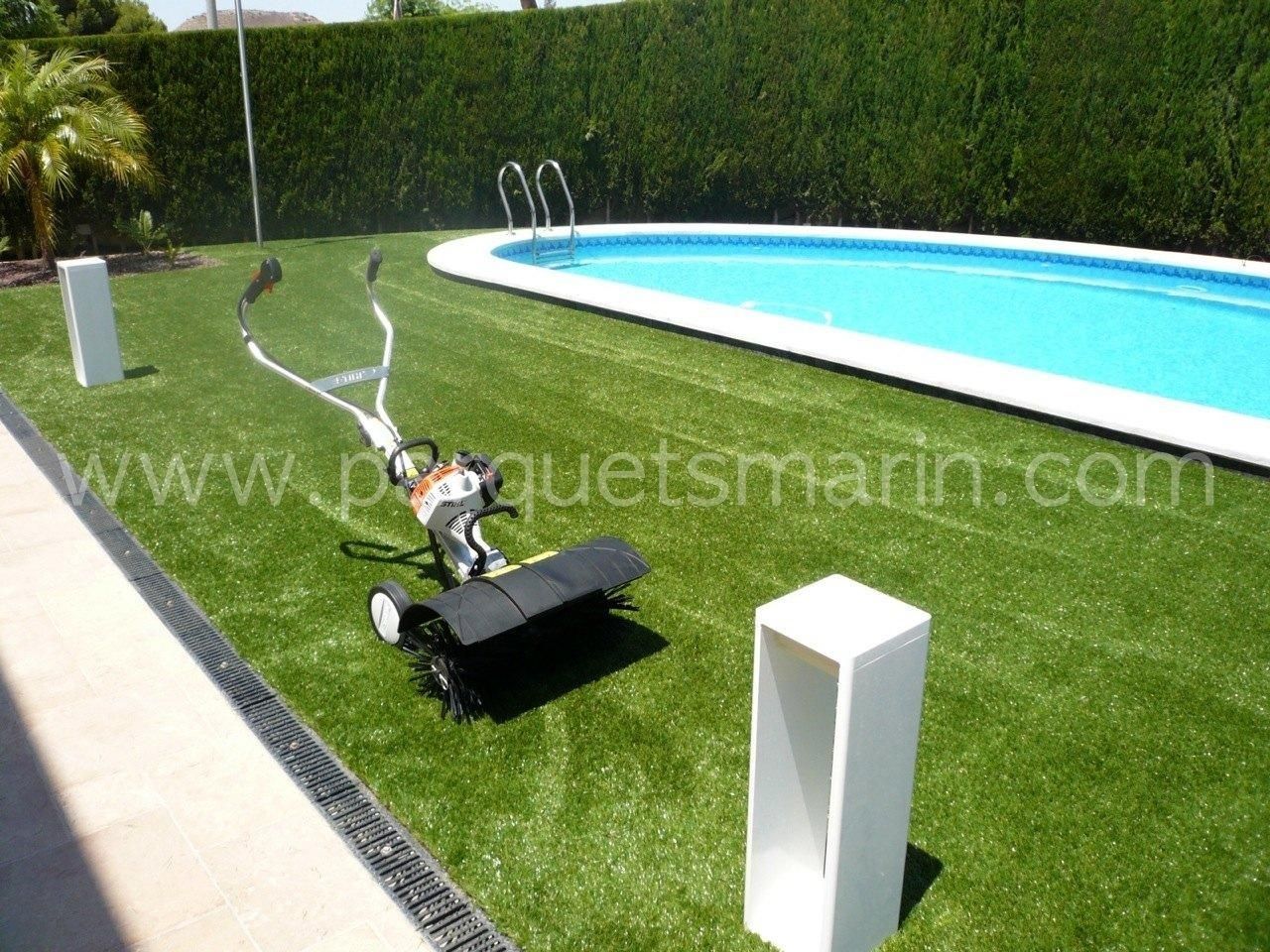 Una cortadora de césped está colocada sobre un exuberante césped verde junto a una piscina.