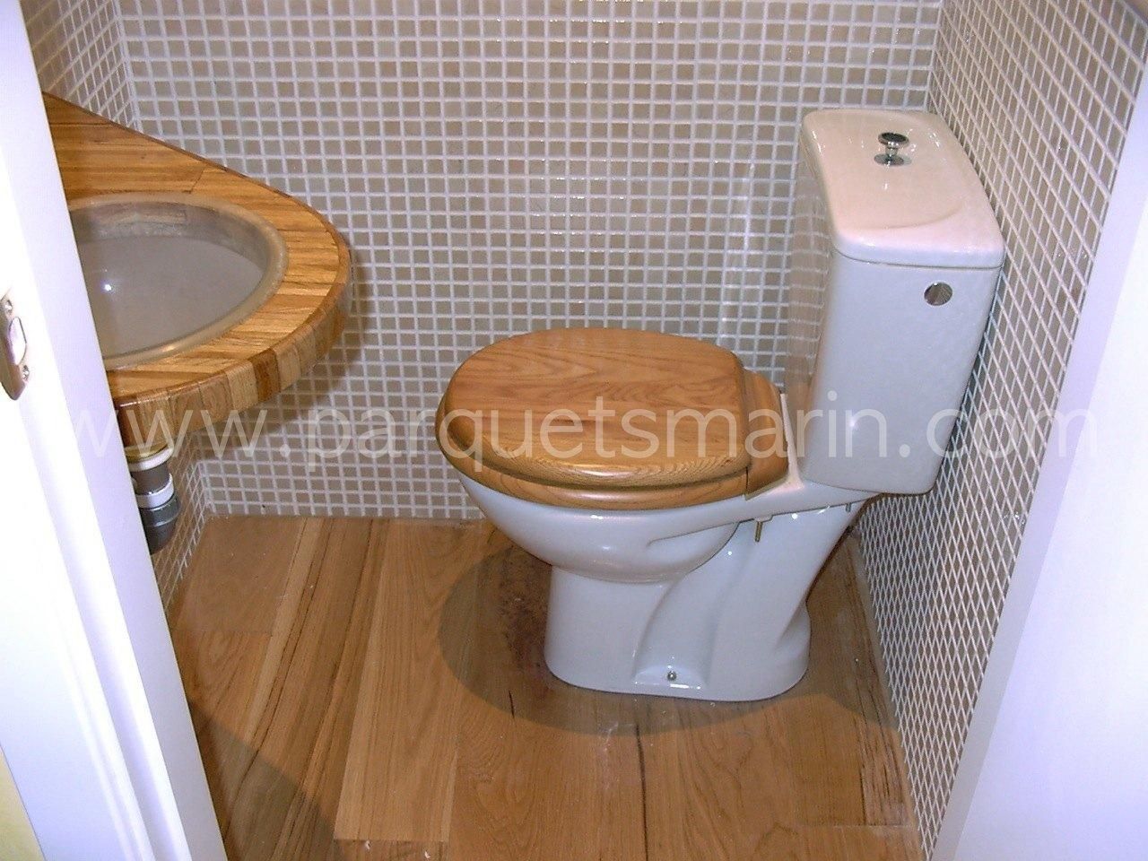 Un inodoro con asiento de madera se encuentra en un baño junto a un lavabo.