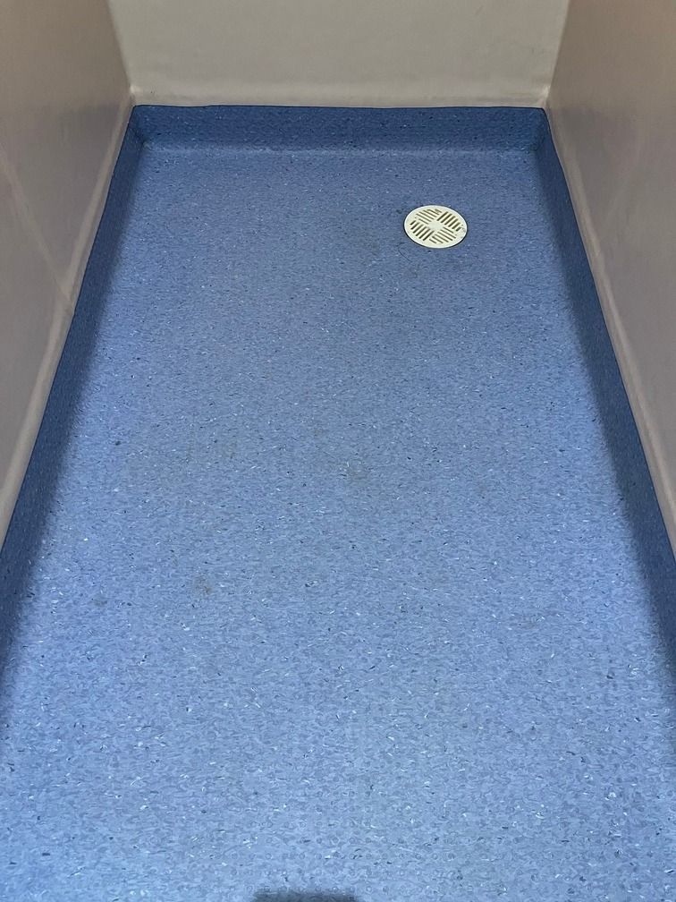 Un baño con suelo azul y desagüe blanco.