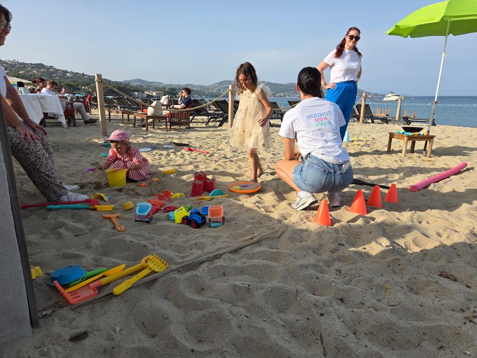 Des enfants jouent avec des jouets de sable sur une plage ; des adultes les surveillent.