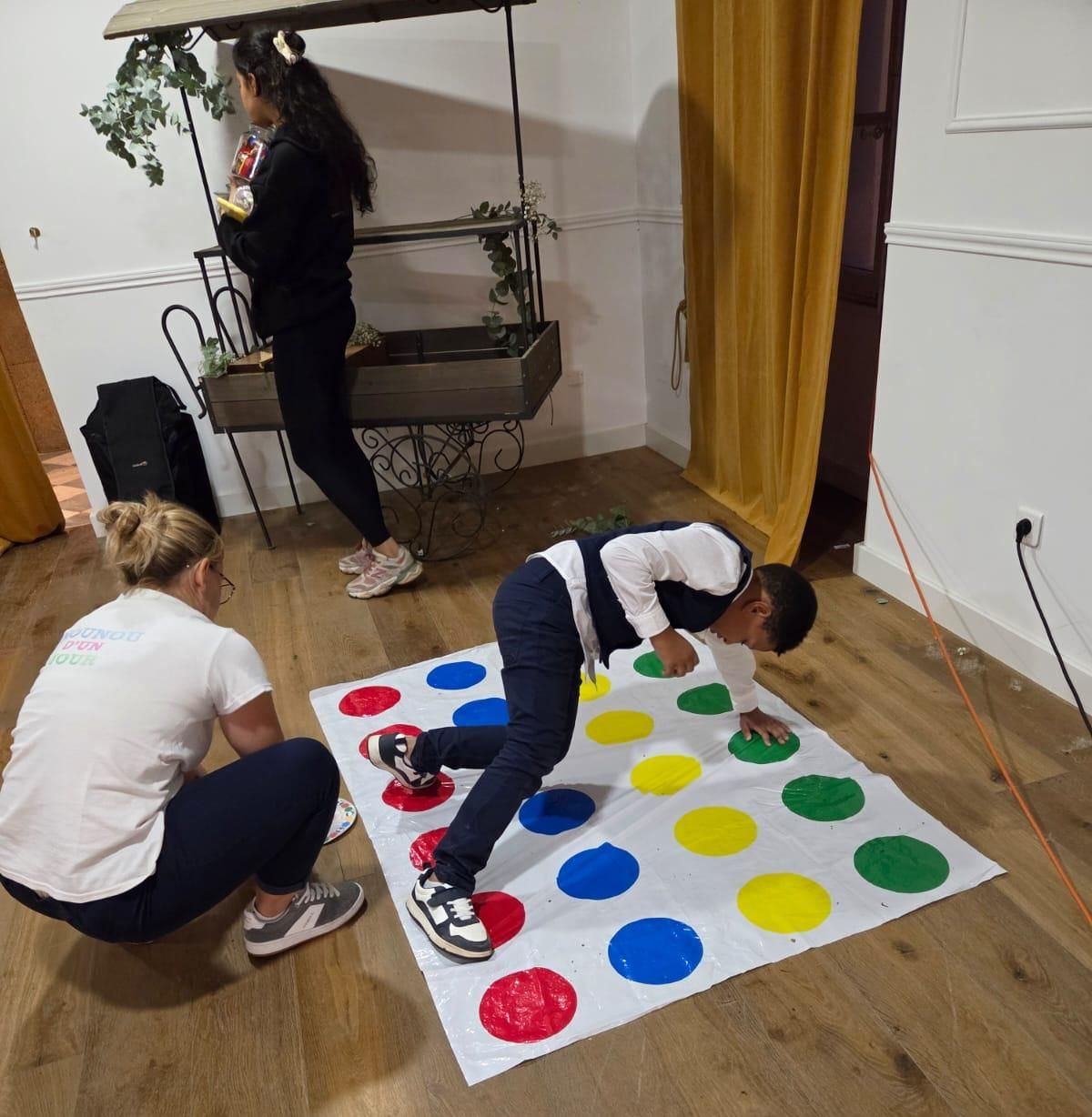 Une personne joue à Twister sur un tapis tandis qu'une autre l'aide.