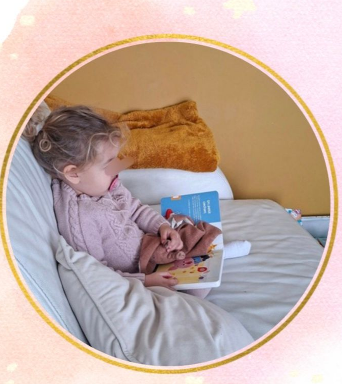 Un jeune enfant au lit, tenant un livre aux pages colorées.