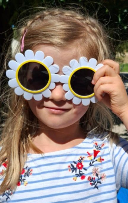 Jeune fille souriante, portant des lunettes de soleil en forme de marguerite.