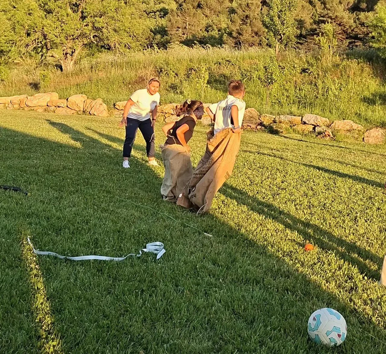 Trois personnes jouent à la course en sac sur une pelouse ; une personne regarde.