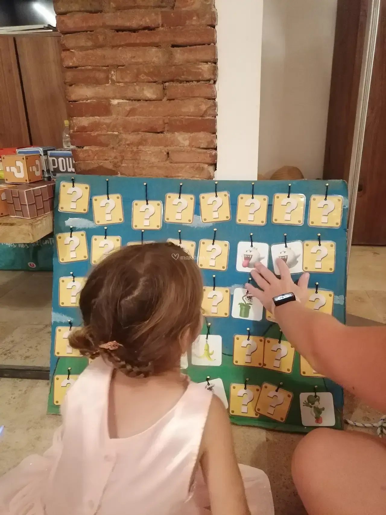 Enfant en robe rose jouant avec un plateau de jeu, la main tendue vers une carte, à l'intérieur.