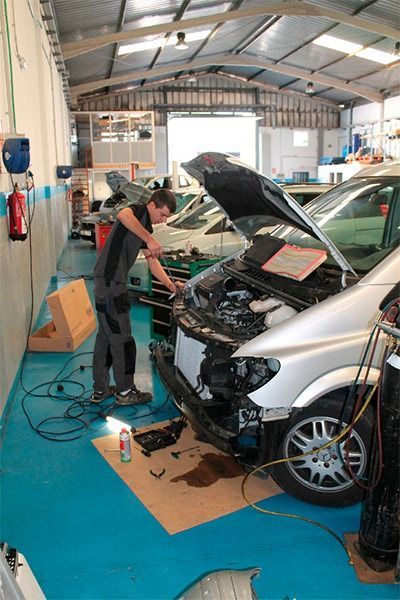 Un hombre está trabajando en un coche en un garaje con el capó abierto.