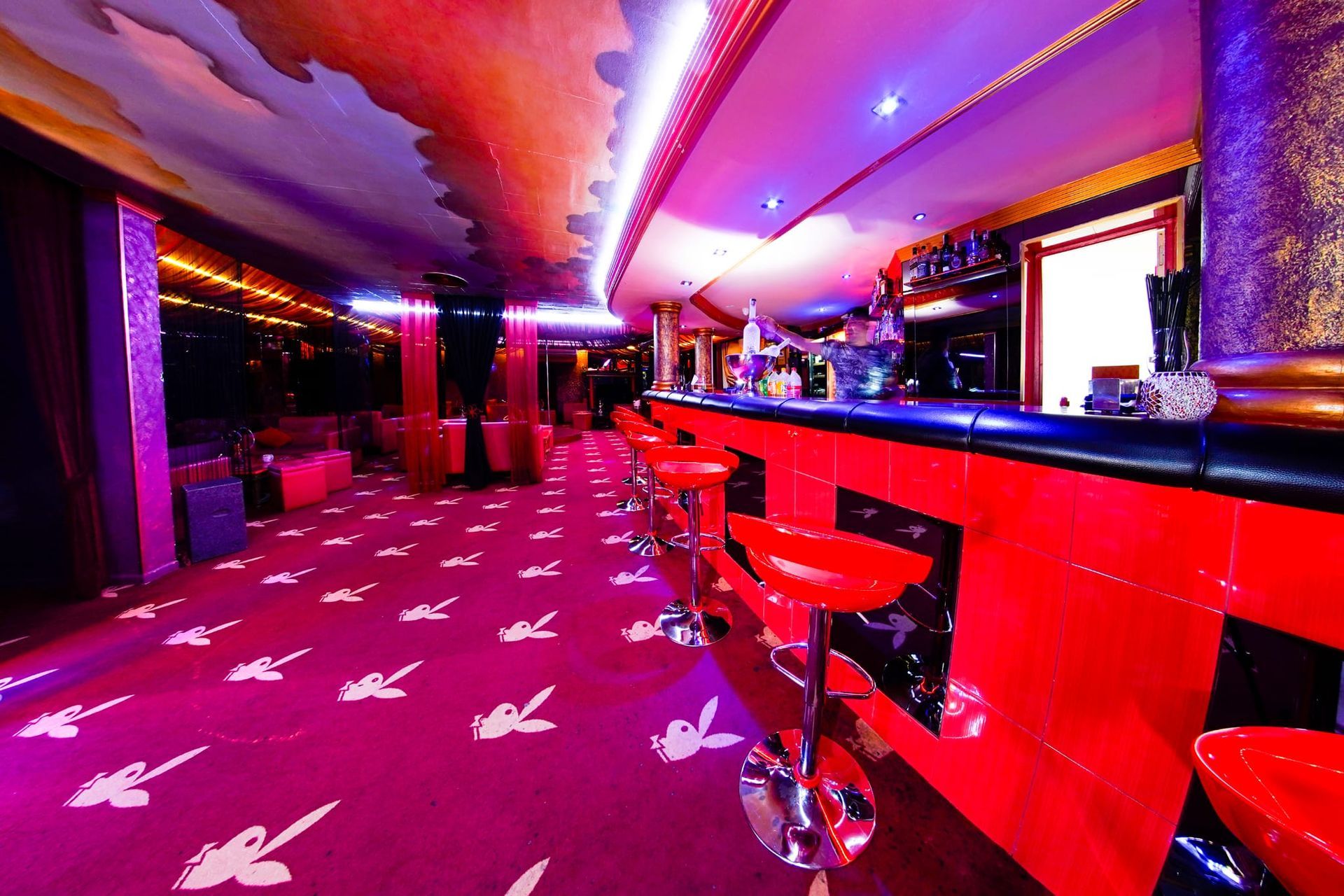 Un bar con taburetes rojos y una alfombra morada.