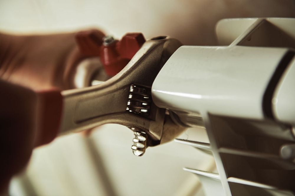 Primer plano de una persona utilizando una llave inglesa ajustable para apretar una válvula en un radiador blanco.