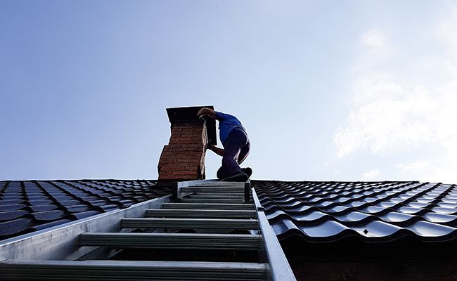 Homme en haut d'une échelle sur une toiture ramonant une cheminée