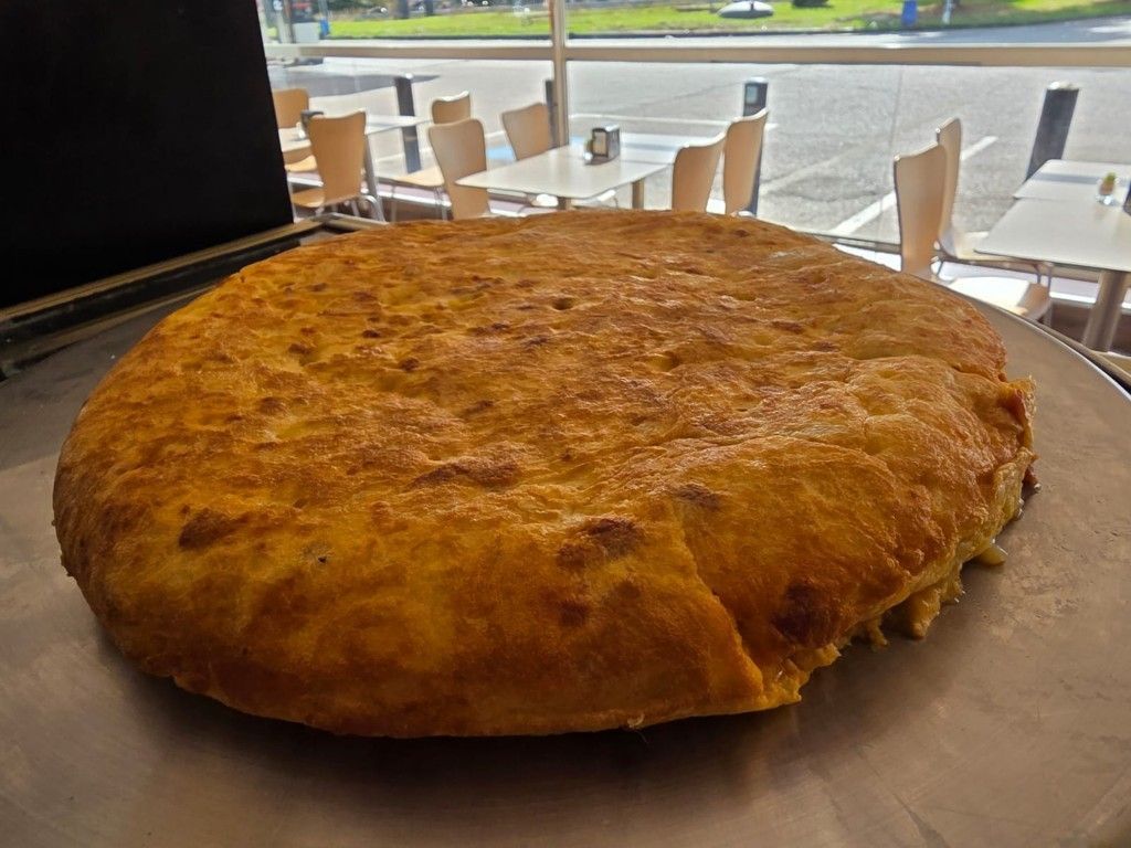 Un gran plato horneado de color marrón dorado sobre una bandeja en una luminosa cafetería junto a la ventana.