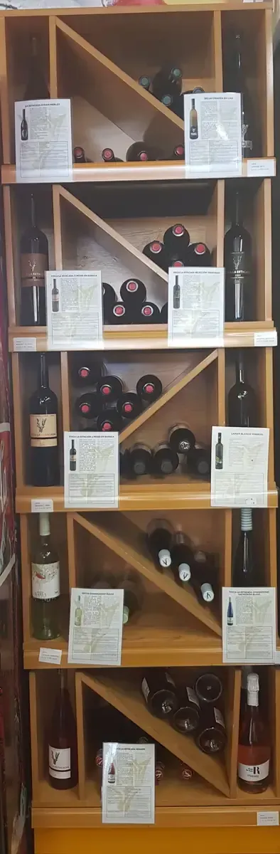 Botellero de madera con botellas variadas y etiquetas blancas en una tienda o bodega.
