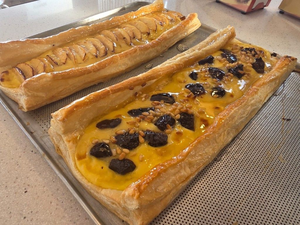 Dos tartaletas de frutas sobre una encimera, una amarilla con frutos rojos oscuros y otra con rodajas de manzana.