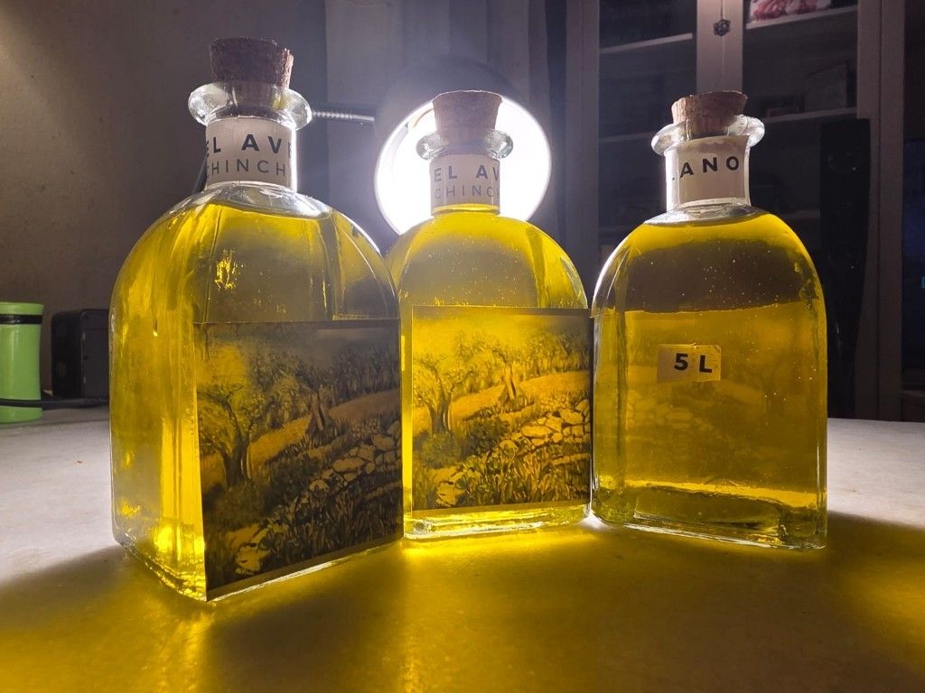 Tres botellas de vidrio llenas de líquido amarillo, etiquetadas como AVC, NC y 5L, sobre una mesa bajo una lámpara brillante.