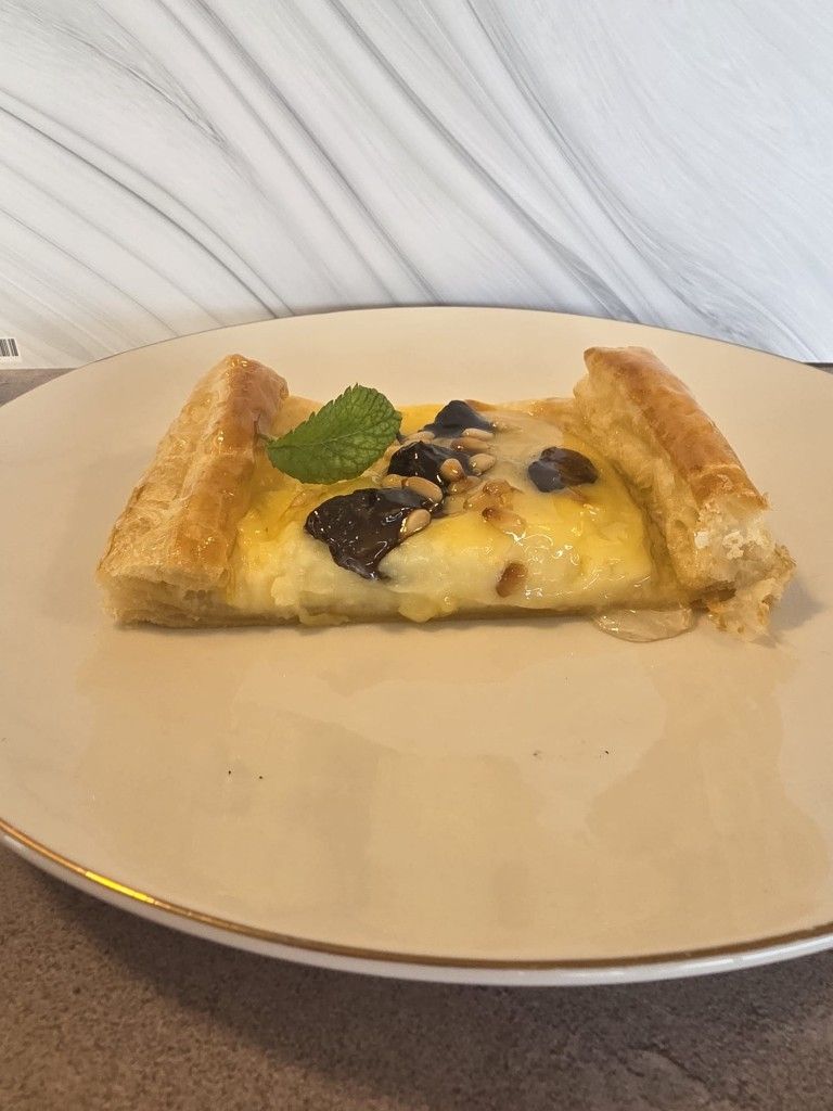 Tarta de hojaldre con crema pastelera, cubierta con arándanos, pepitas de chocolate y una hoja de menta, servida en un plato.