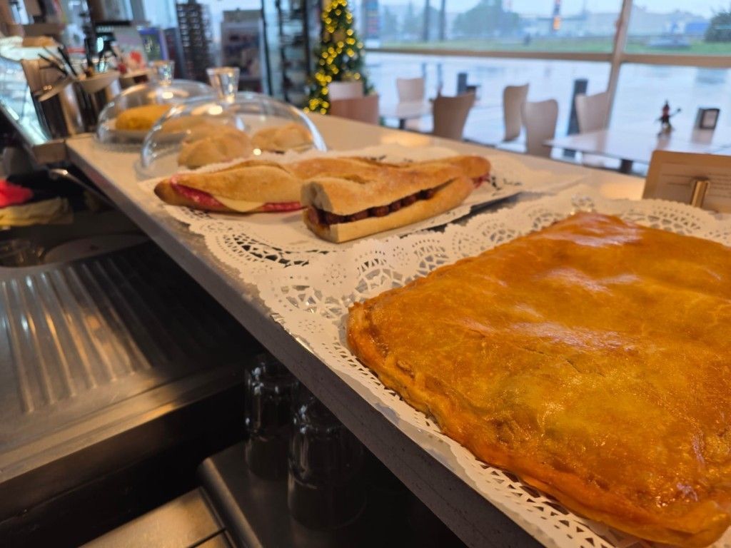 Pasteles en el mostrador de una cafetería junto a una ventana con vistas al agua y a los edificios de la ciudad.