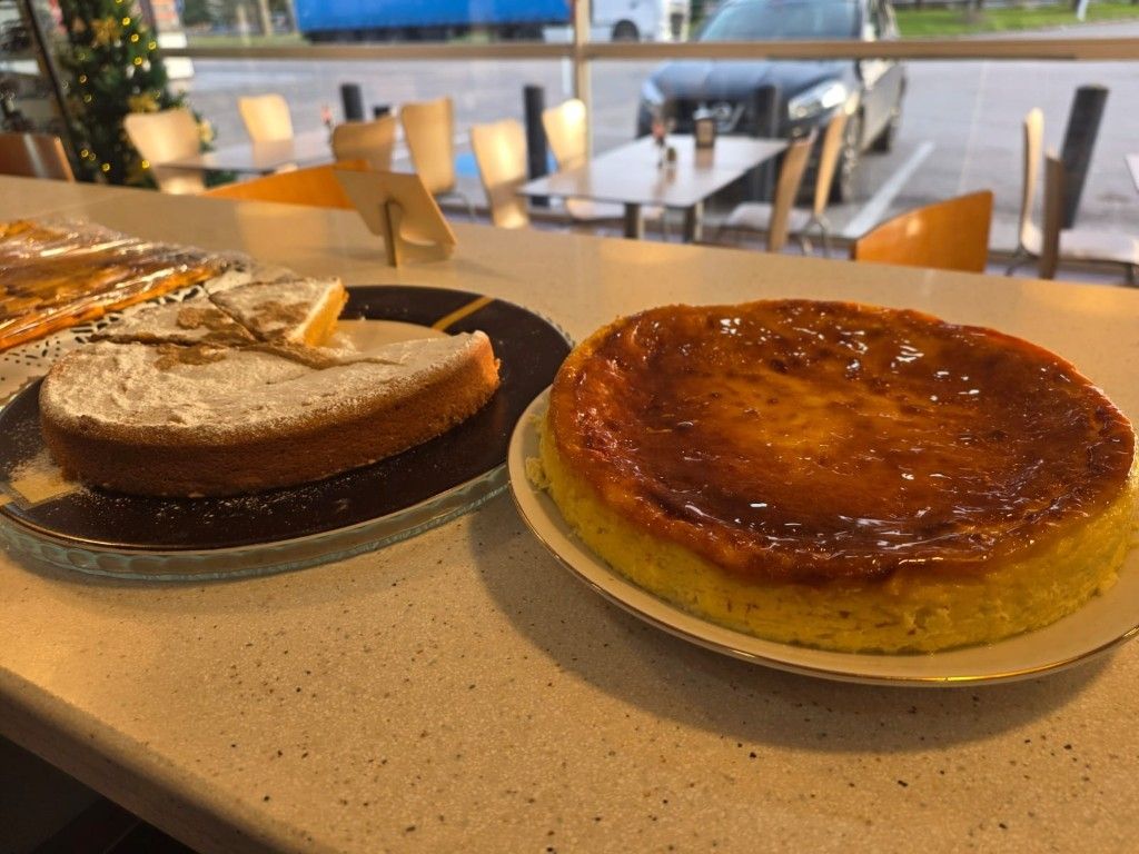 Dos postres en platos sobre la mesa de una cafetería: un pastel de chocolate y un flan de caramelo brillante.