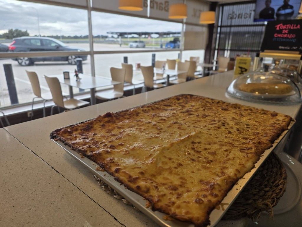 Una gran pizza rectangular de queso sobre una mesa junto a una ventana en un restaurante luminoso.