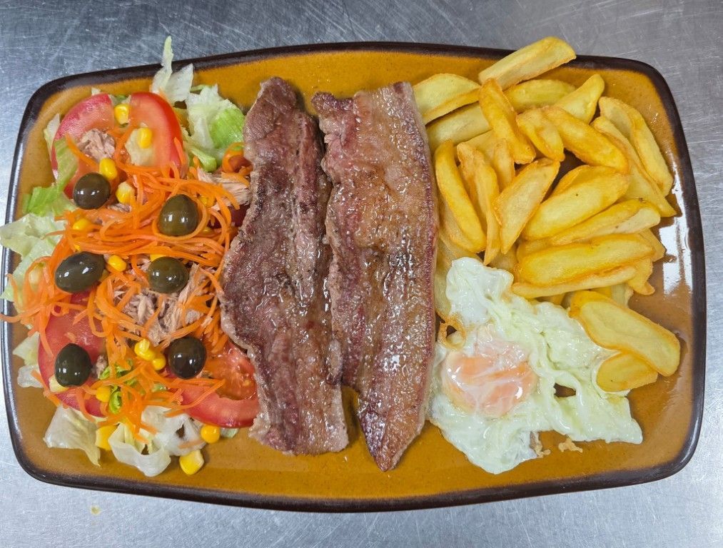 Filete a la parrilla con papas fritas y ensalada en un plato rectangular.