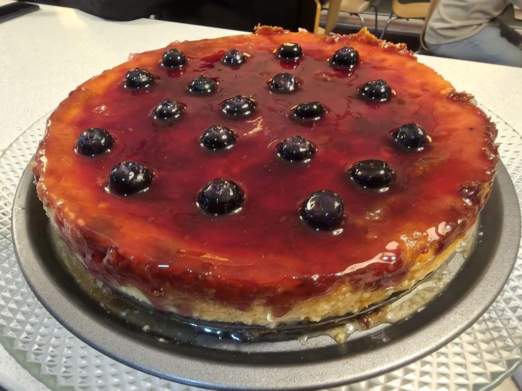 Tarta de queso con cerezas glaseadas y arándanos, servida en un plato de plata.