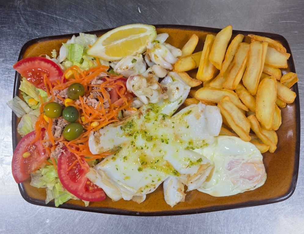 Ensalada mixta con limón y patatas fritas en un plato rectangular.