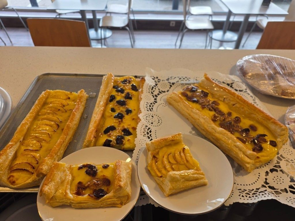 Pasteles de frutas variados en bandejas y platos en un ambiente de cafetería.