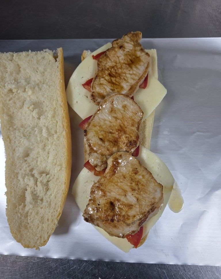 Sándwich abierto con pollo a la parrilla y queso envuelto en papel de aluminio, acompañado de un panecillo rebanado.